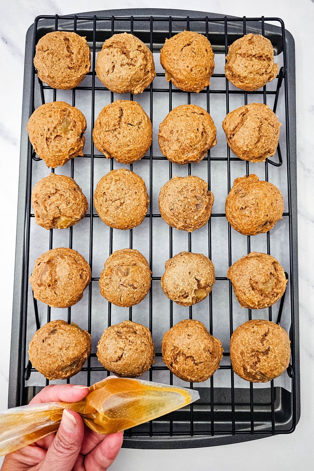 Drizzling caramel sauce from a piping bag over baked apple cookies on a rack
