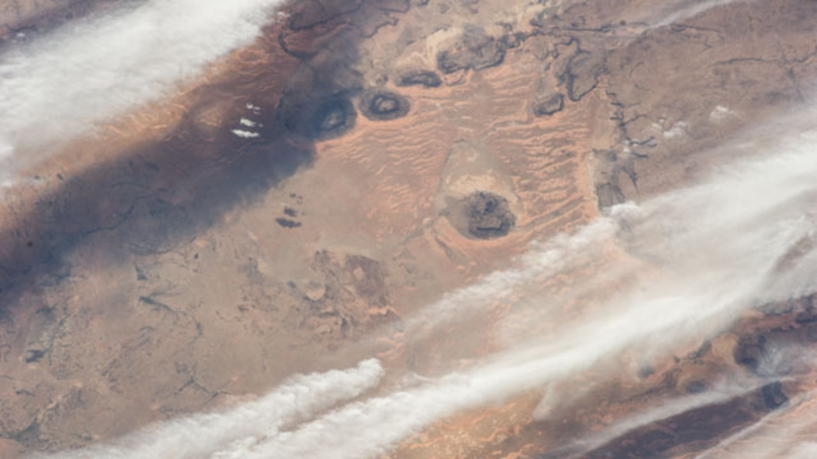 This astronaut photo, taken in 2014, shows that the three mesas and their dunes are part of a much larger system leftover from an ancient Paleozoic feature. Credit: NASA/ISS program