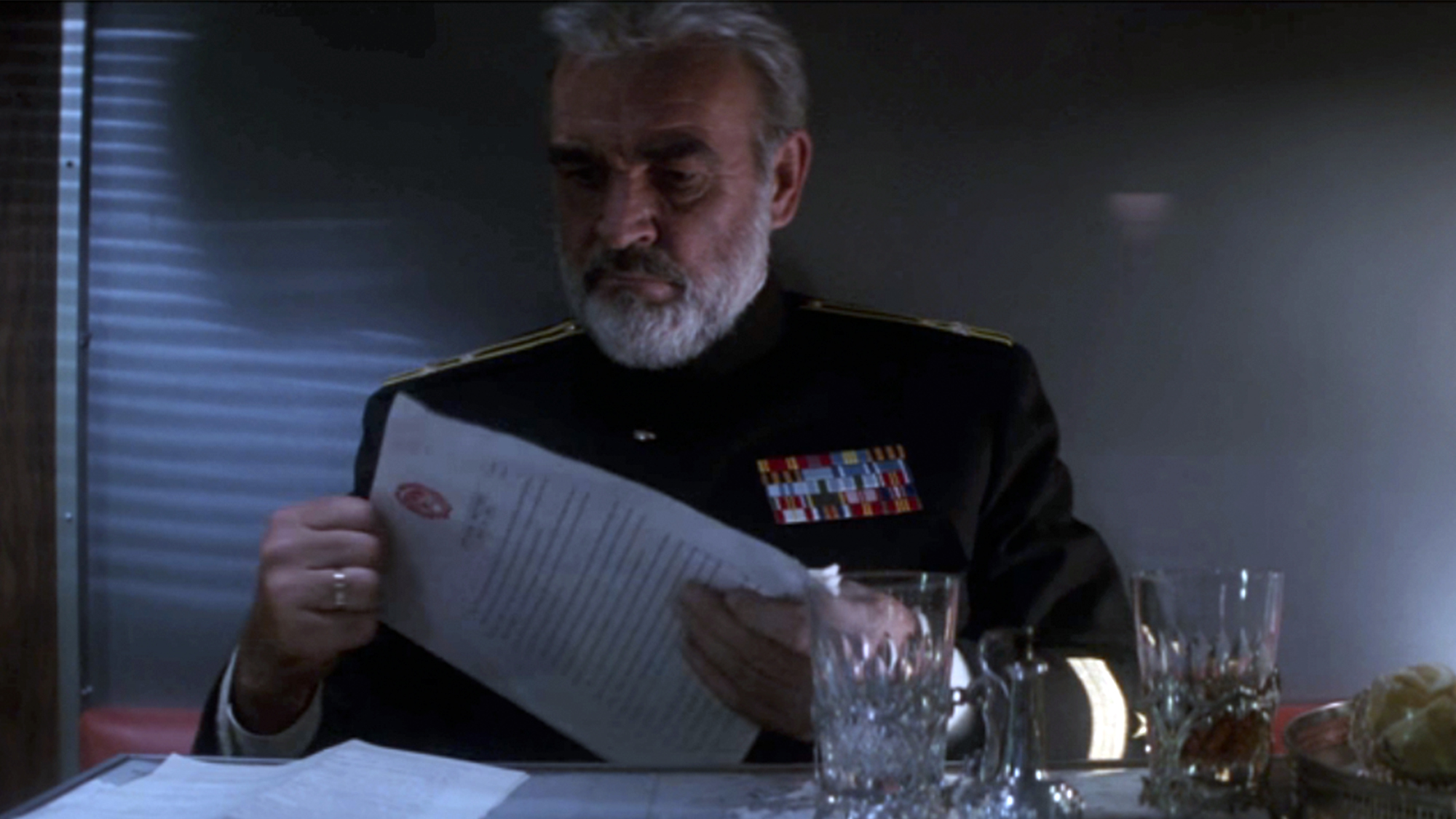 Sean Connery holding a piece of paper and sitting at a table in The Hunt for Red October