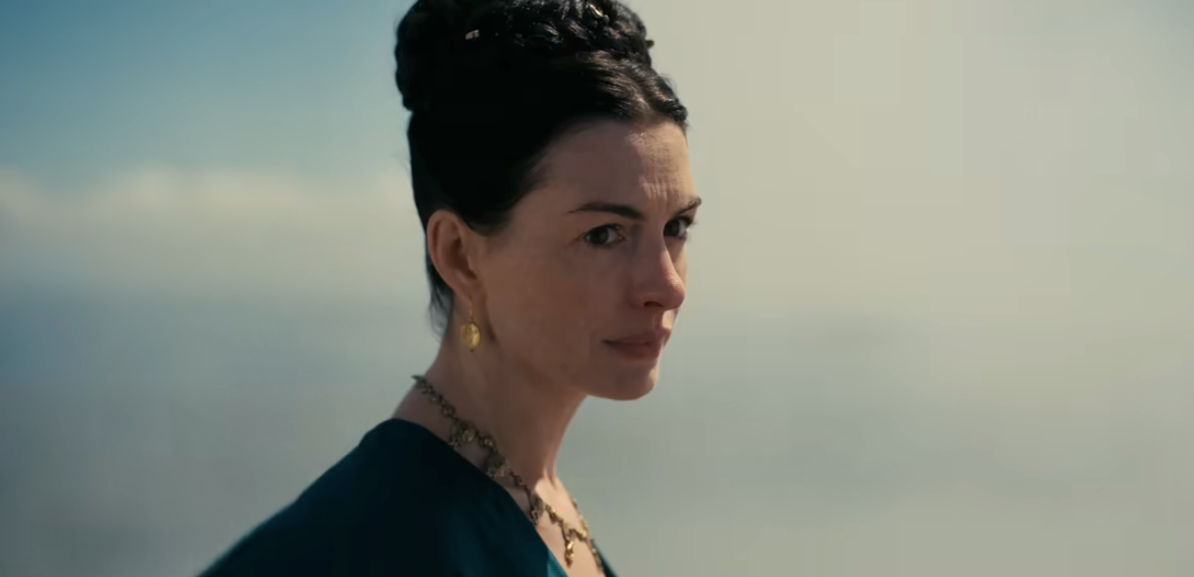 Person with a thoughtful expression, wearing a high-neck top and a necklace, looking towards the distance in an outdoor setting