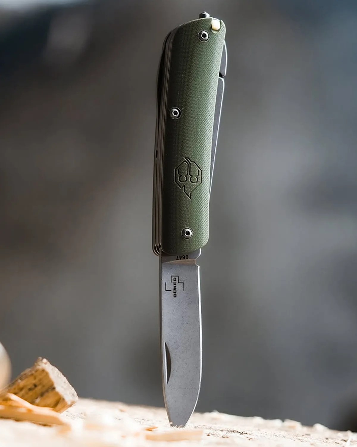 Folding knife with a green textured handle and a partially open stainless steel blade standing upright on a wooden surface.