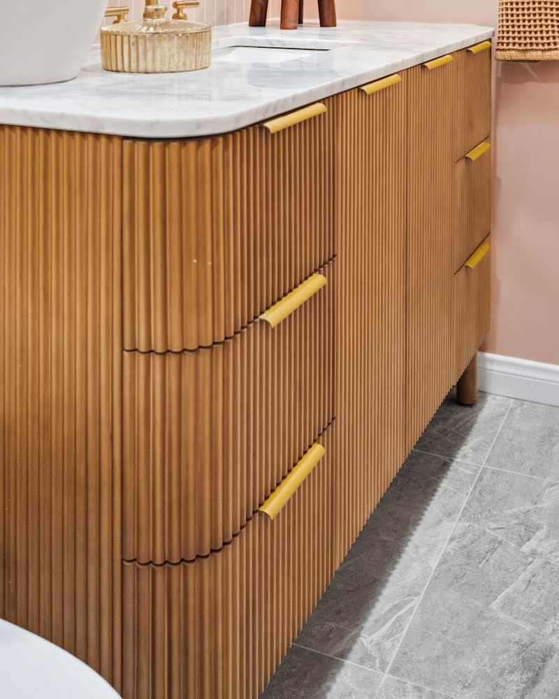 Stylish modern bathroom vanity unit. The design includes fluted wood cabinetry, a premium marble countertop, and unique yellow handles.