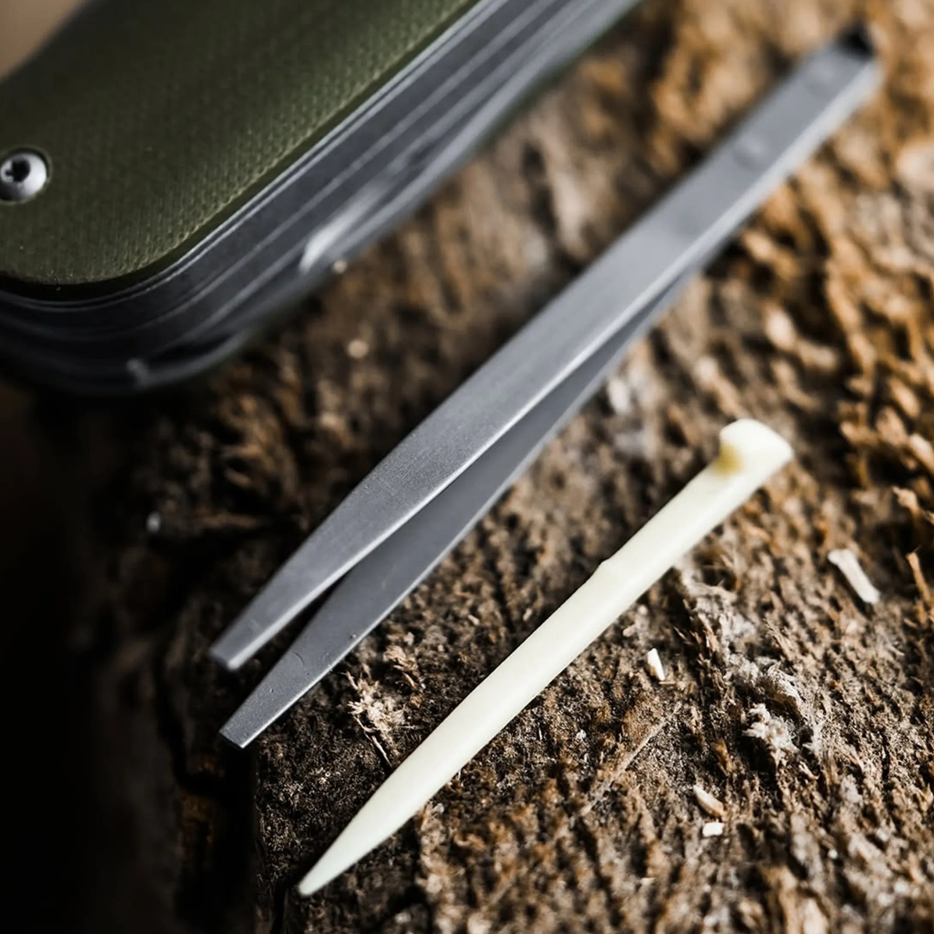 Close-up of metal tweezers and a white bone needle on a textured brown surface.