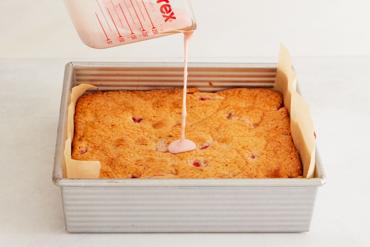 Strawberry glaze being poured over a baked pan of strawberry brownies