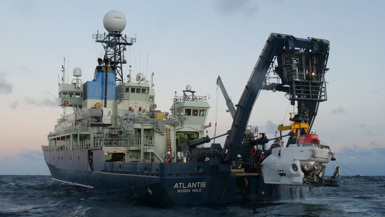ship with an arm lifting a white submersible vehicle