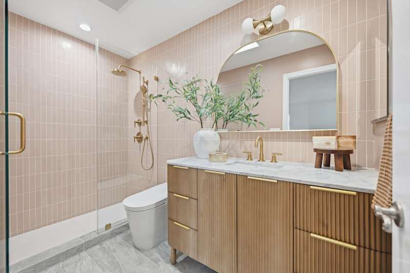 Interior shot of a luxury contemporary bathroom featuring a fluted white vanity, striking pink vertical tiling, and elegant brass hardware fixtures.