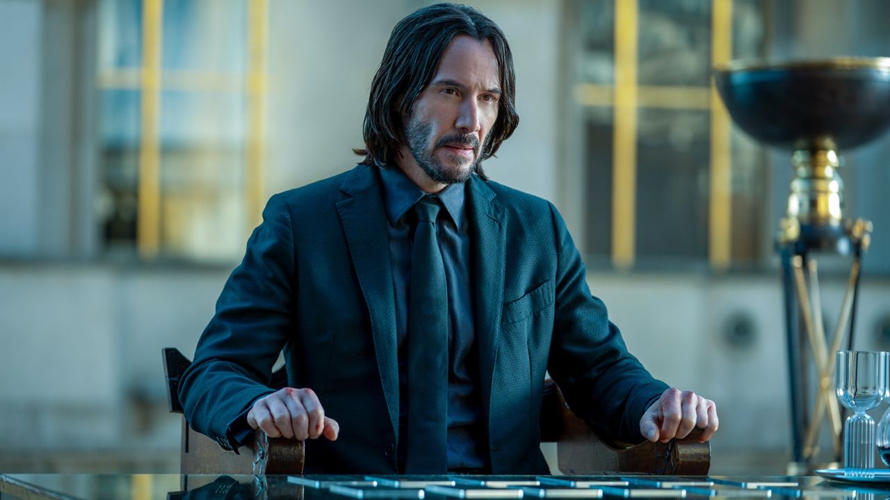 John (Keanu Reeves) sits at a table in John Wick: Chapter 4.