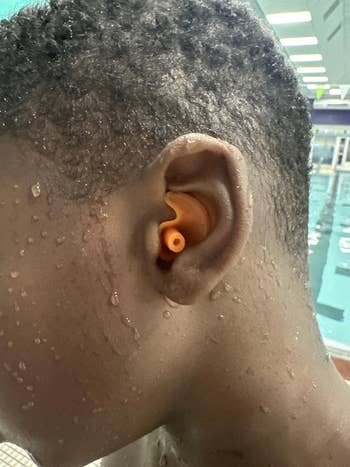 Close-up of a person wearing an orange earplug in a pool, with water droplets on their skin