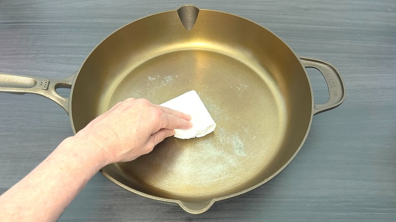 Hand spreading cooking oil onto the bottom of Made In seasoned cast iron 12" skillet with a paper towel