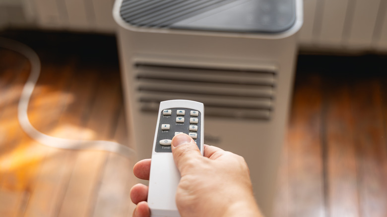 A person using a remote to control an air cooler in the background.