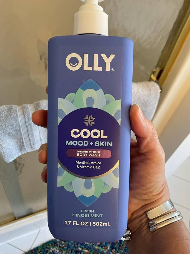 Person holding a bottle of OLLY Cool Mood + Skin Body Wash, featuring menthol, arnica, and vitamin B12 in a 17 fl oz size