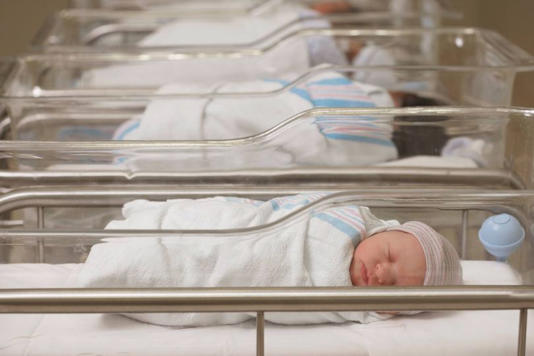 Several newborns are lying in incubators, which are enclosed in transparent glass enclosures, arranged in a row.