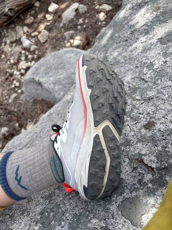 A hiking shoe with a rugged sole on a rocky terrain, paired with a grey sock featuring a mountain outline