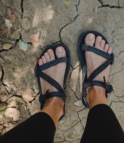 Person wearing minimalist sandals on cracked earth, highlighting outdoor footwear style