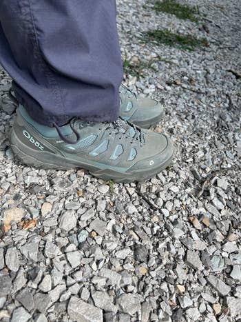 Person wearing gray hiking shoes and gray pants stands on a gravel path
