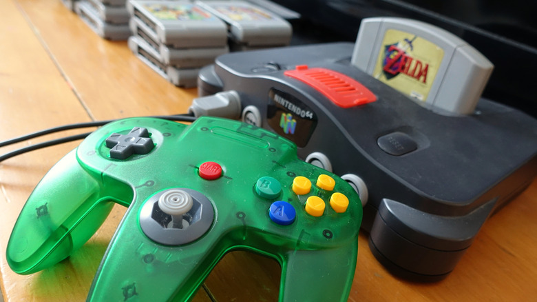 Green Nintendo 64 controller plugged into a Nintendo 64 console with The Legend of Zelda cartridge inserted.