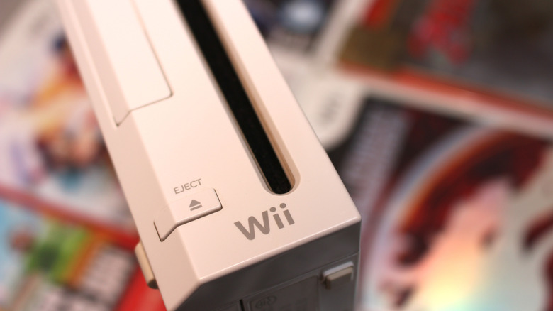 Nintendo Wii console close-up with the disc slot and eject button visible against blurred game cases.