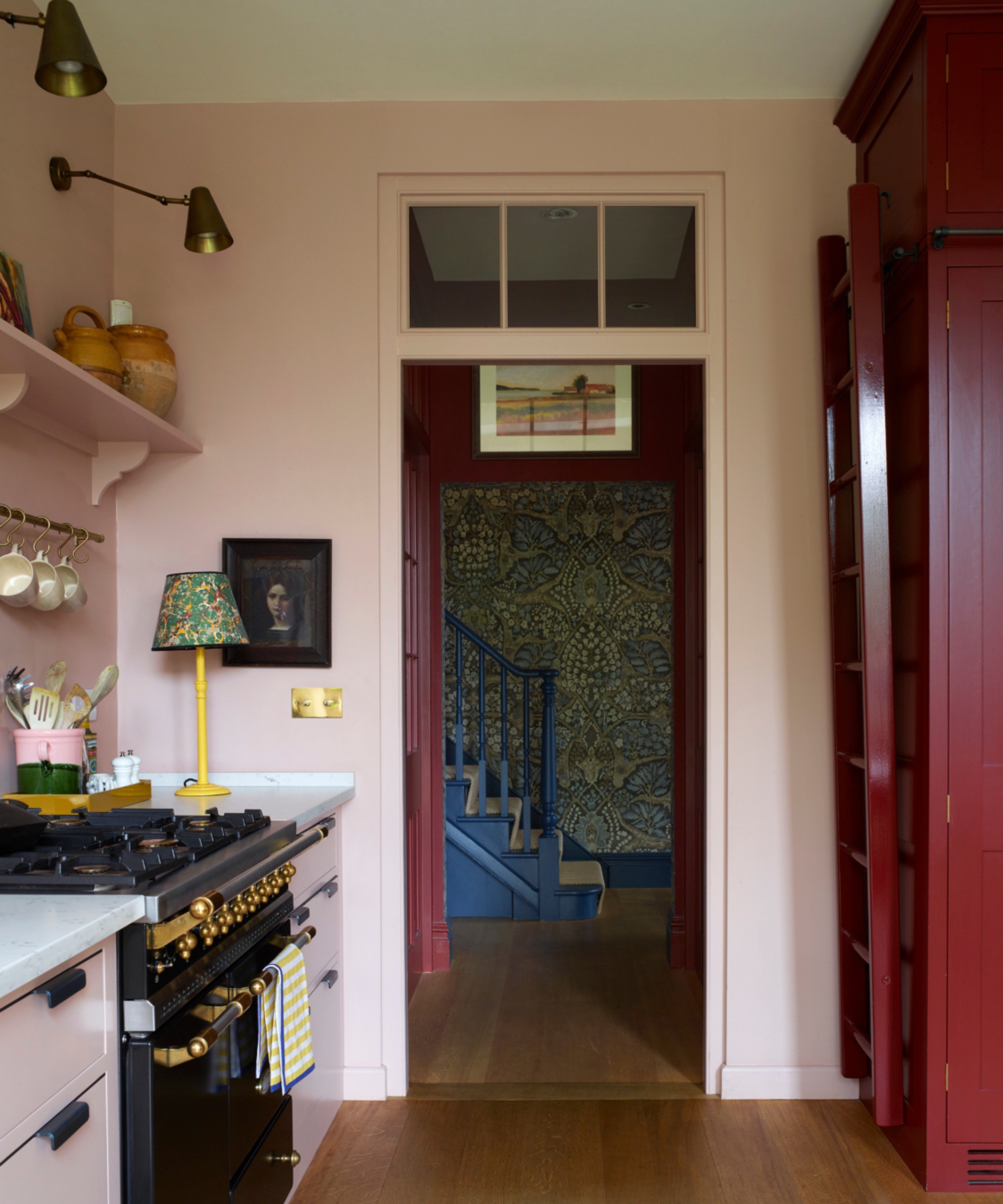 A pink kitchen with brass wall lights and a bright yellow counter lamp with a green patterned lamp shade