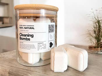 Jar of 100% natural cleaning bombs with a label showing ingredients and usage instructions on a countertop