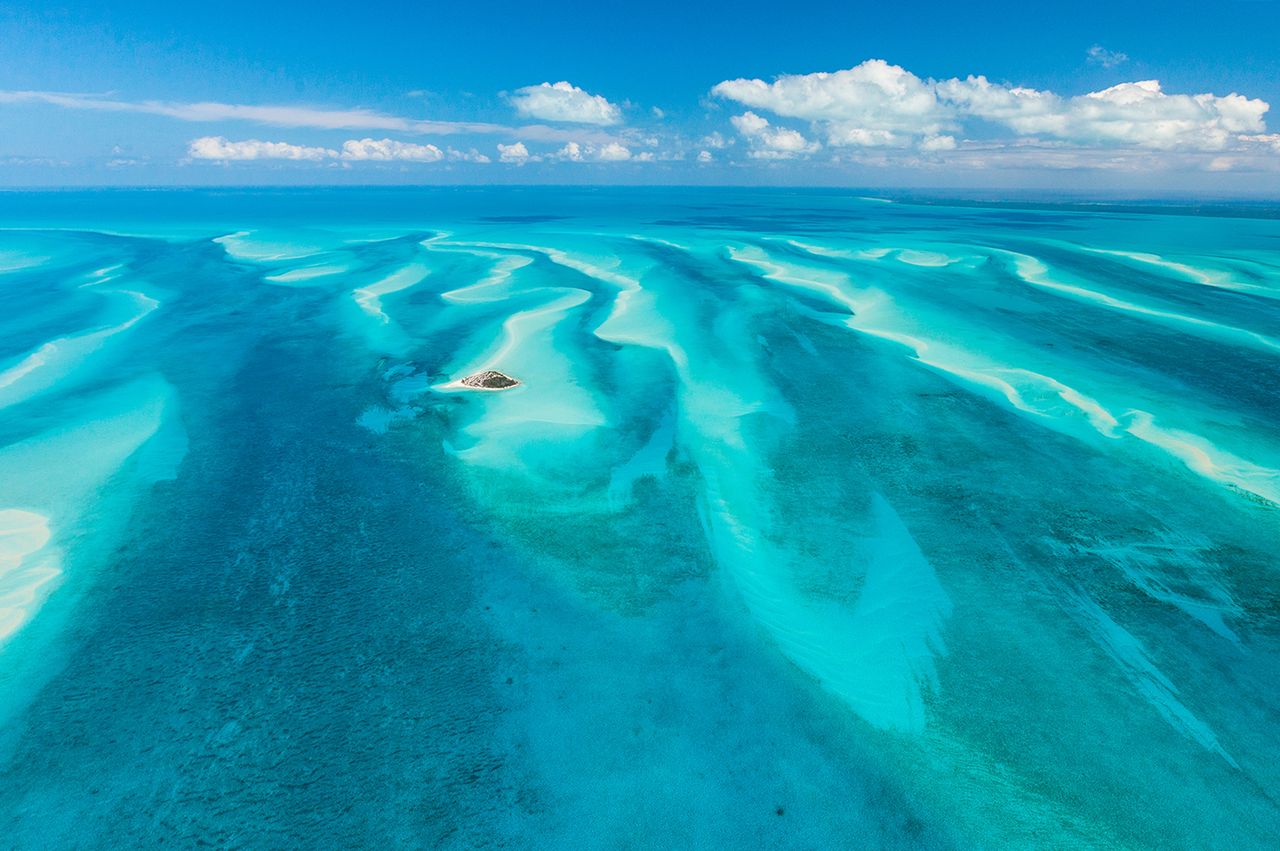 Aerial view of a small island surrounded by shallow sandbanks and clear blue water