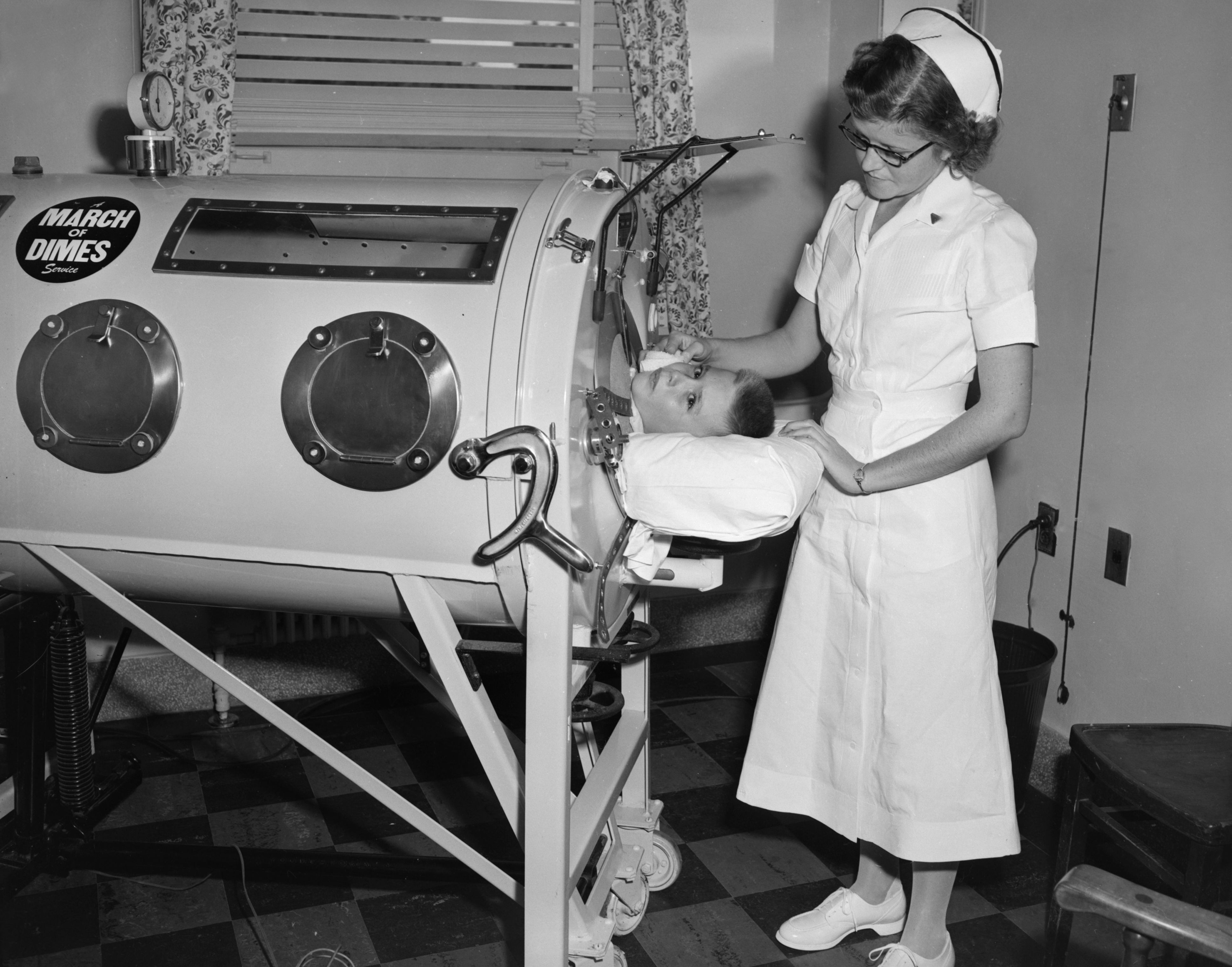 A nurse in a vintage uniform tends to a child in an iron lung, with a March of Dimes sticker visible. The setting appears to be a medical facility