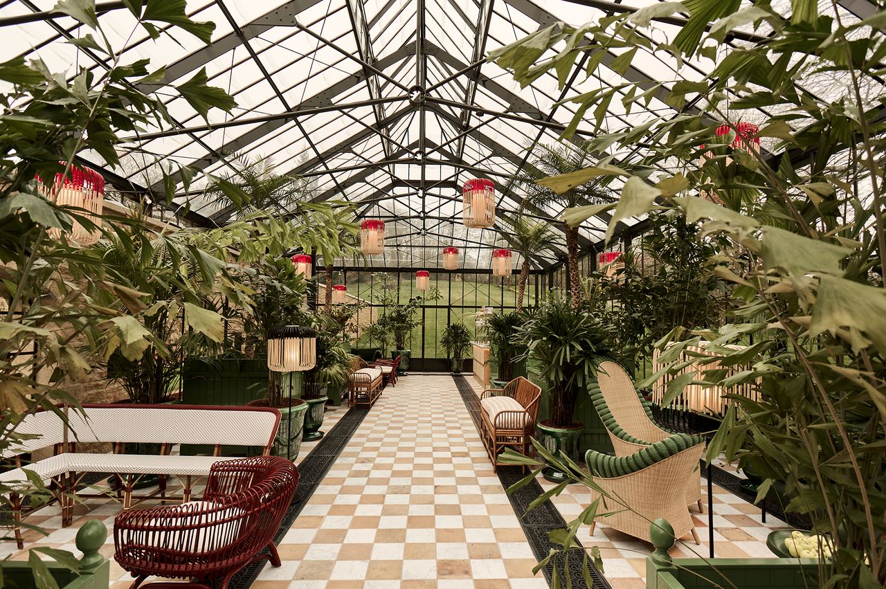 Interior of a glasshouse with plants and seating arrangements along a tiled pathway