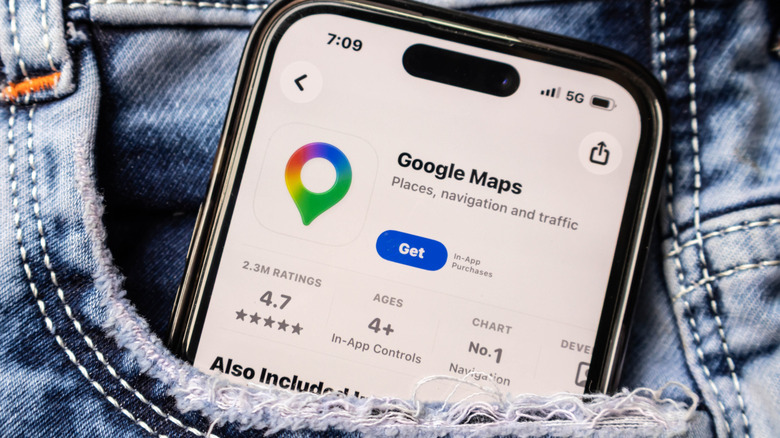 A smartphone displaying the Google Maps page within an app store as the device peaks out of the frayed front pocket of a pair of jeans