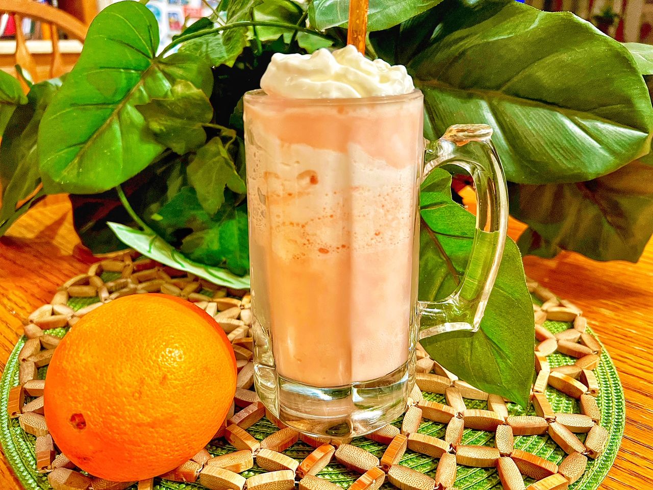 orange creamsicle shake in clear tall glass with orange on beaded mat