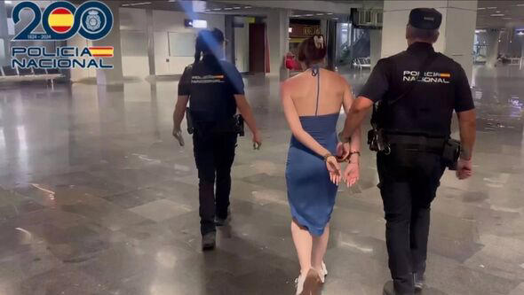 An individual dressed in a blue dress and wearing handcuffs is being escorted by two individuals in black uniforms, likely law e