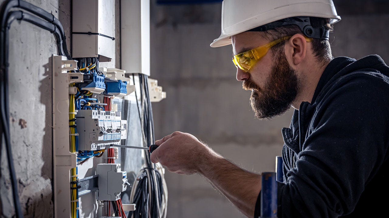 An electrician works on a switchboard with an electrical connecting cable, connects the equipment with tools.