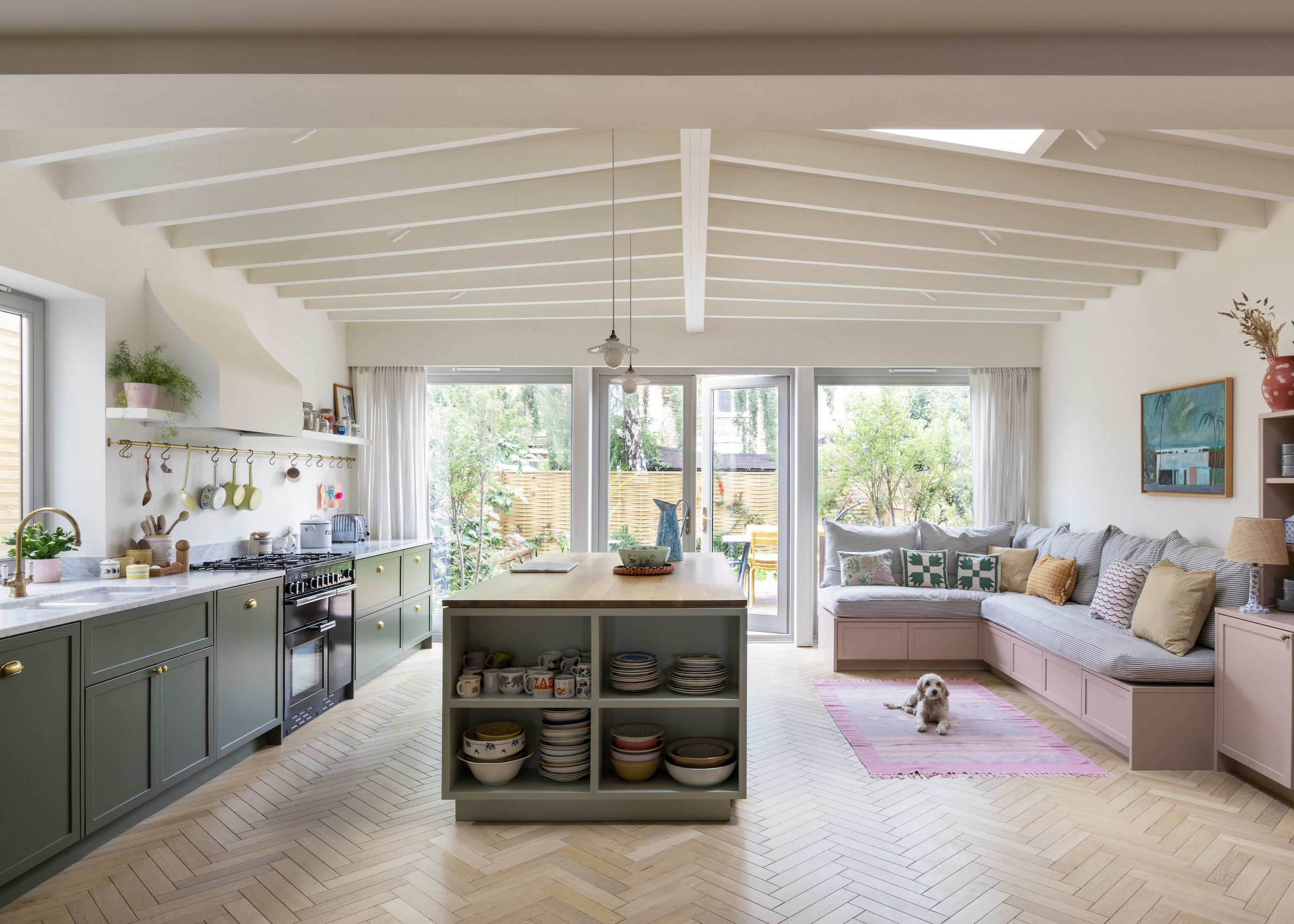 a large kitchen extension with an open plan layout, with green cabinets and an island on one side, and pink cabinets with a banquette on the other