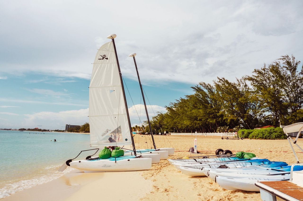 Sailboats and kayaks on a sandy beach by a calm sea with trees along the shoreline