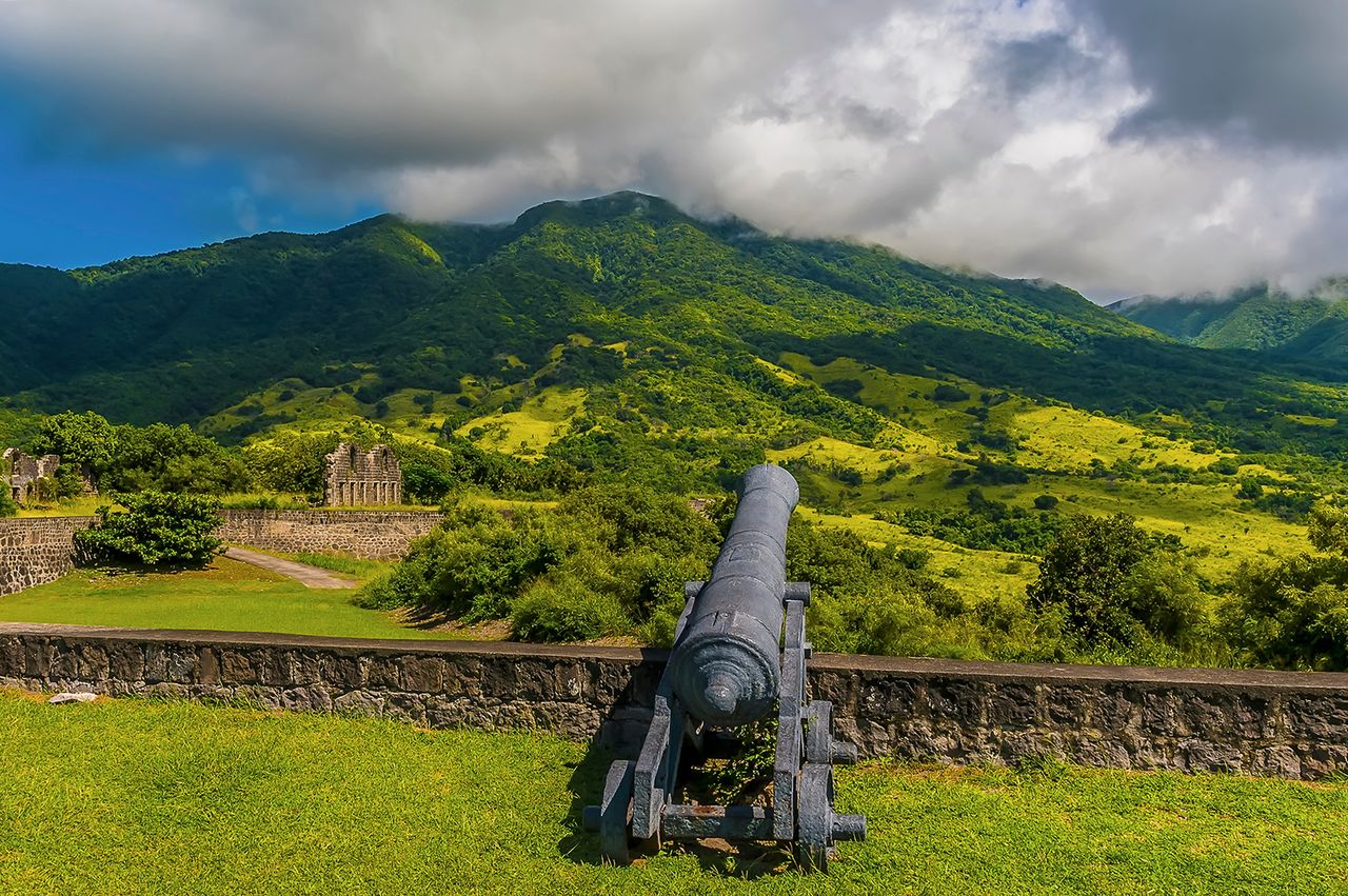 A historical cannon overlooking lush green hills and ruins on St Kitts