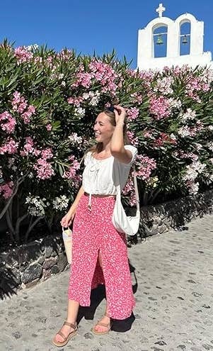 reviewer smiling in a white blouse and patterned skirt with Teva sandals, standing on a cobblestone path,