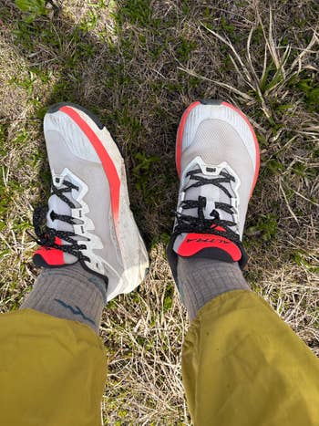 Person wearing stylish athletic sneakers with distinct laces, standing on grass, paired with casual pants