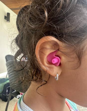 Child wearing pink silicone earplugs, focusing on right ear with curls