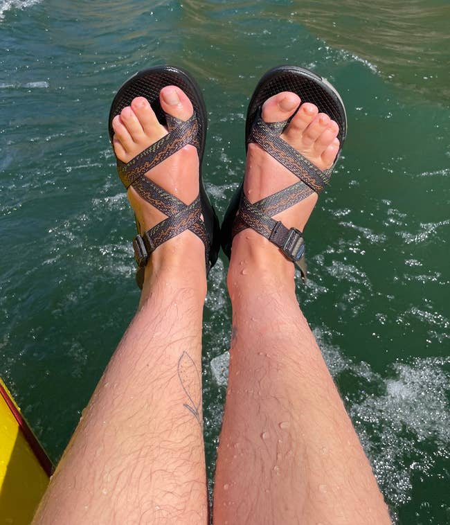 Feet wearing sandals are over water, suggesting a relaxing outdoor setting. Suitable for summer activities or vacation shopping articles