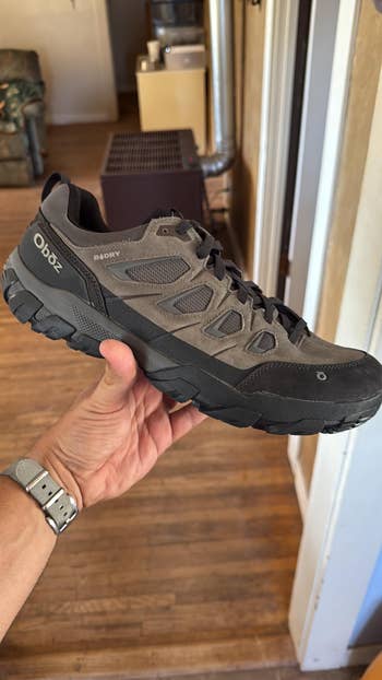 A hand holds a rugged hiking shoe with a durable sole and breathable mesh, ideal for outdoor activities
