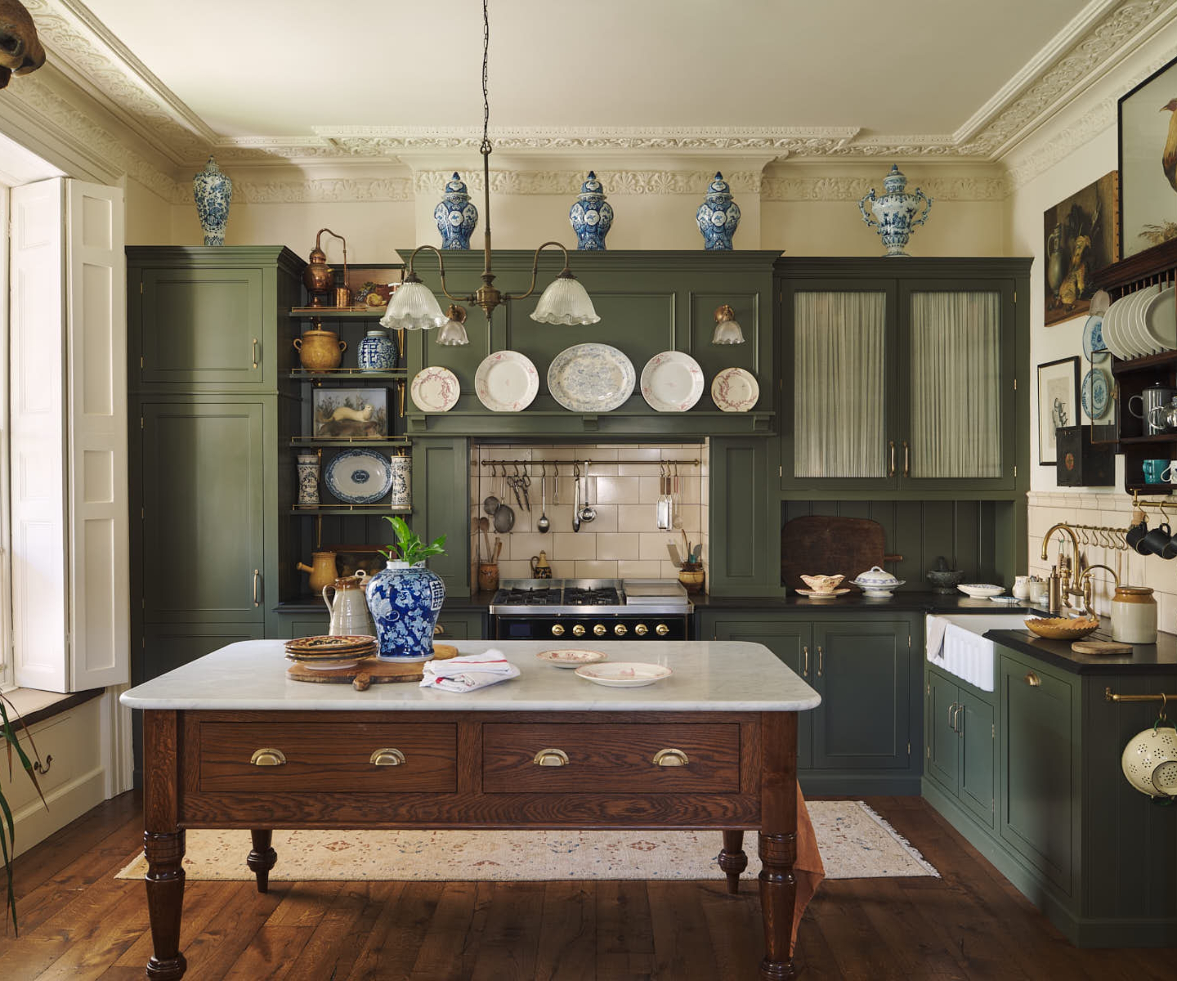 A dark green kitchen with mixed cabinet styles, a freestanding wooden prep table, and an eclectic mix of art