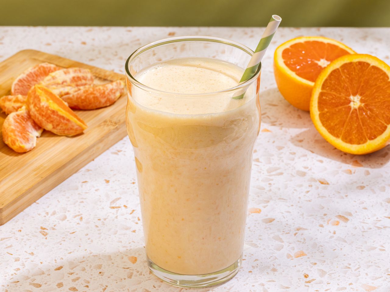 Creamy orange smoothie in tall glass with striped straw.