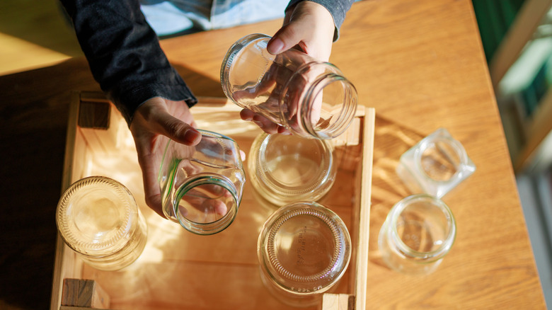 A woman holding some clear glass jars in a wooden crate.