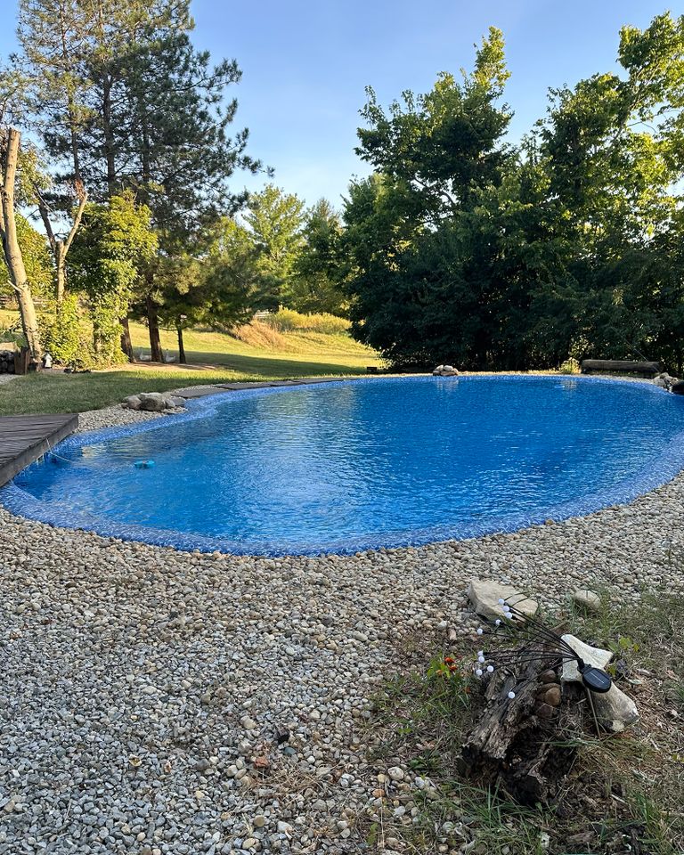 A naturalstyle pool surrounded by trees and gravel