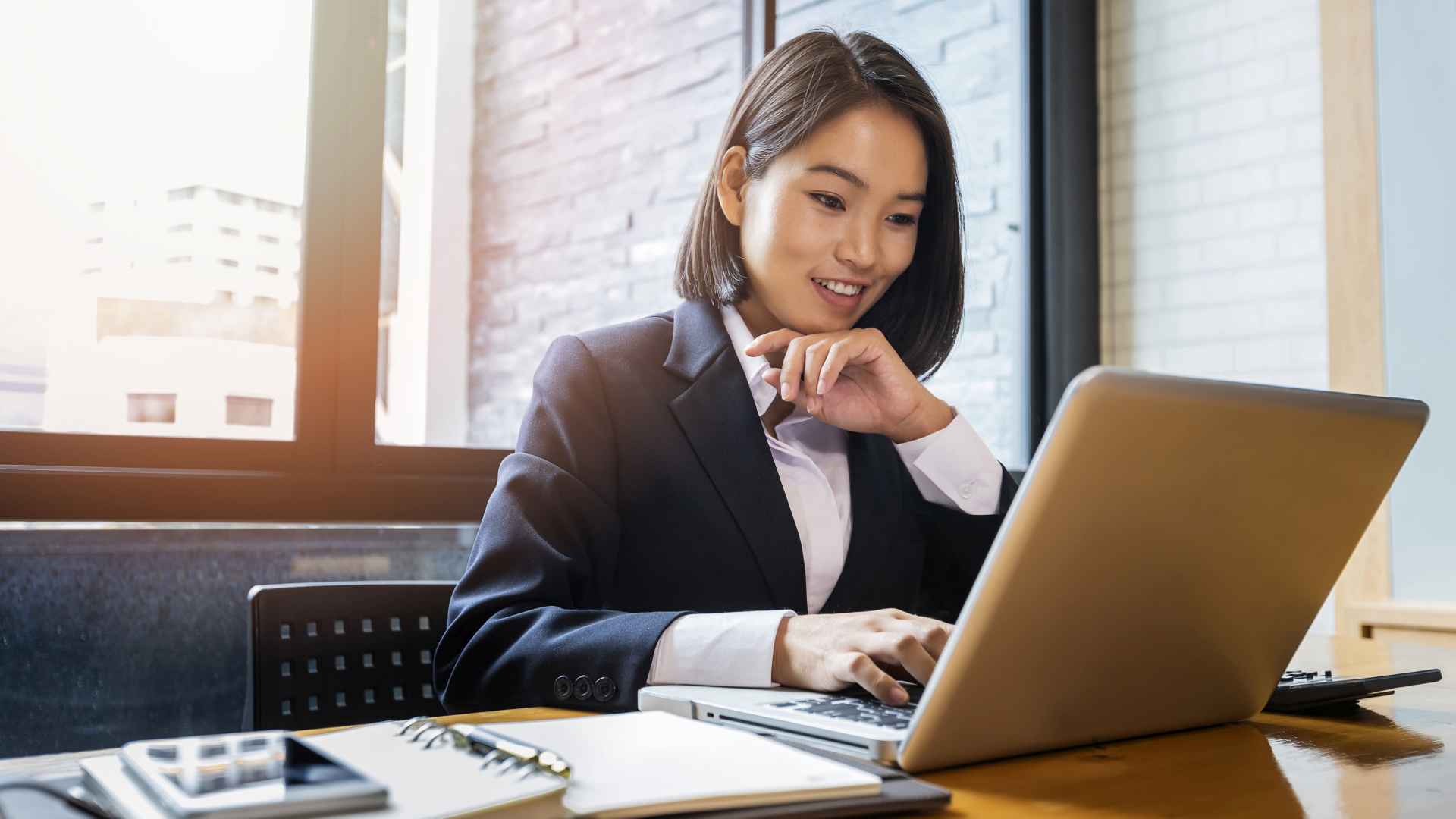 Discover a young Asian businesswoman, using a laptop with a happy or interested expression