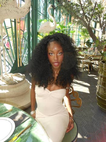 Person in a strapless, form-fitting dress seated at an elegant dining setting with elaborate decor, including large bird sculptures and greenery