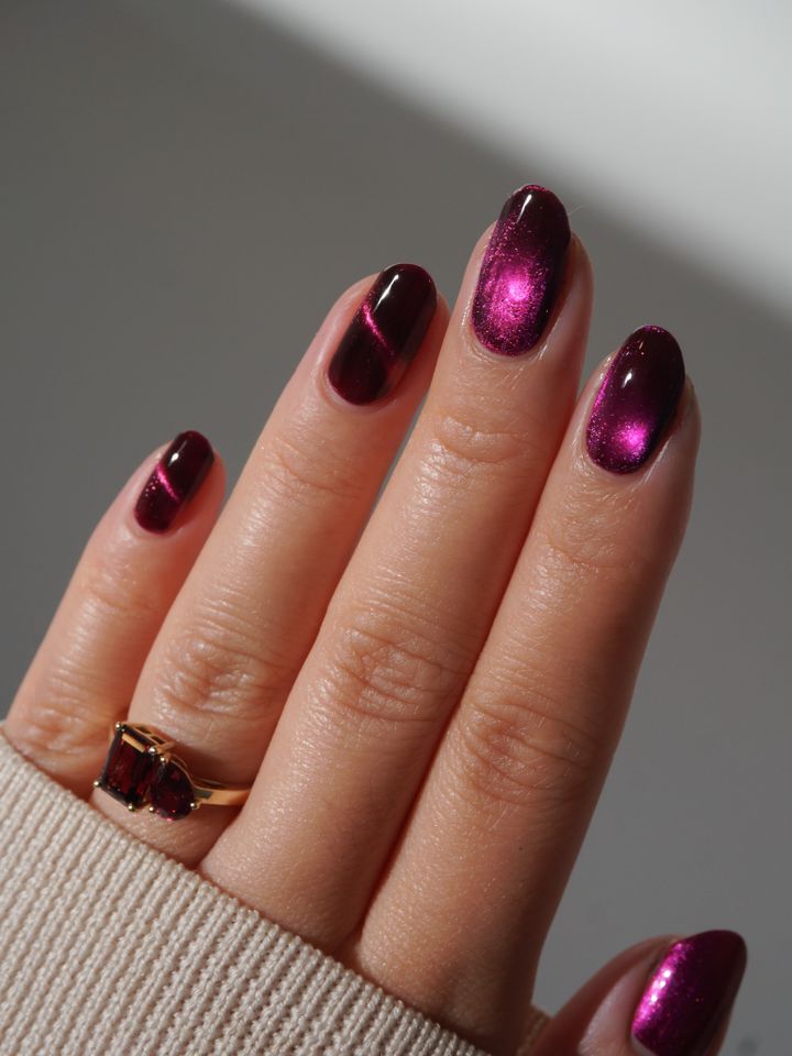 A hand with metallic purple nail polish wearing a gold ring with a stone