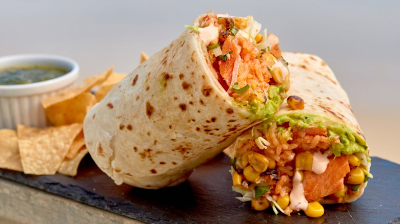 Close up of two halves of a burrito with chips and dip on slate