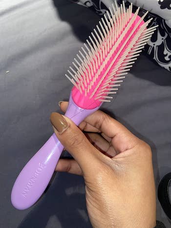 Hand holding a pink and purple Denman hairbrush with nylon bristles, suitable for detangling and styling hair
