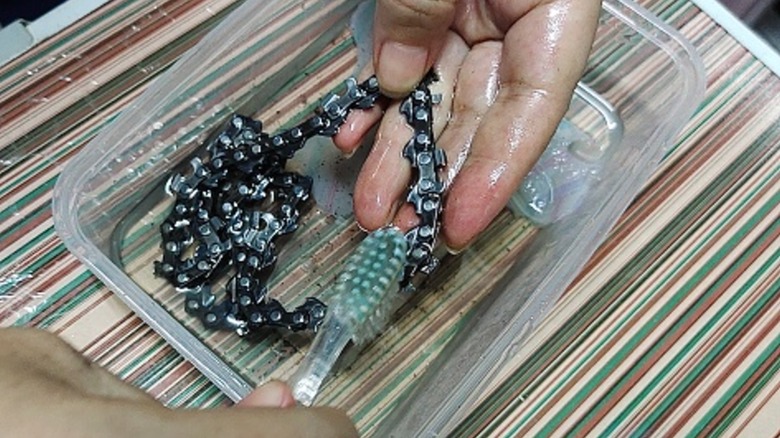 Oily chainsaw chain being cleaned with toothbrush