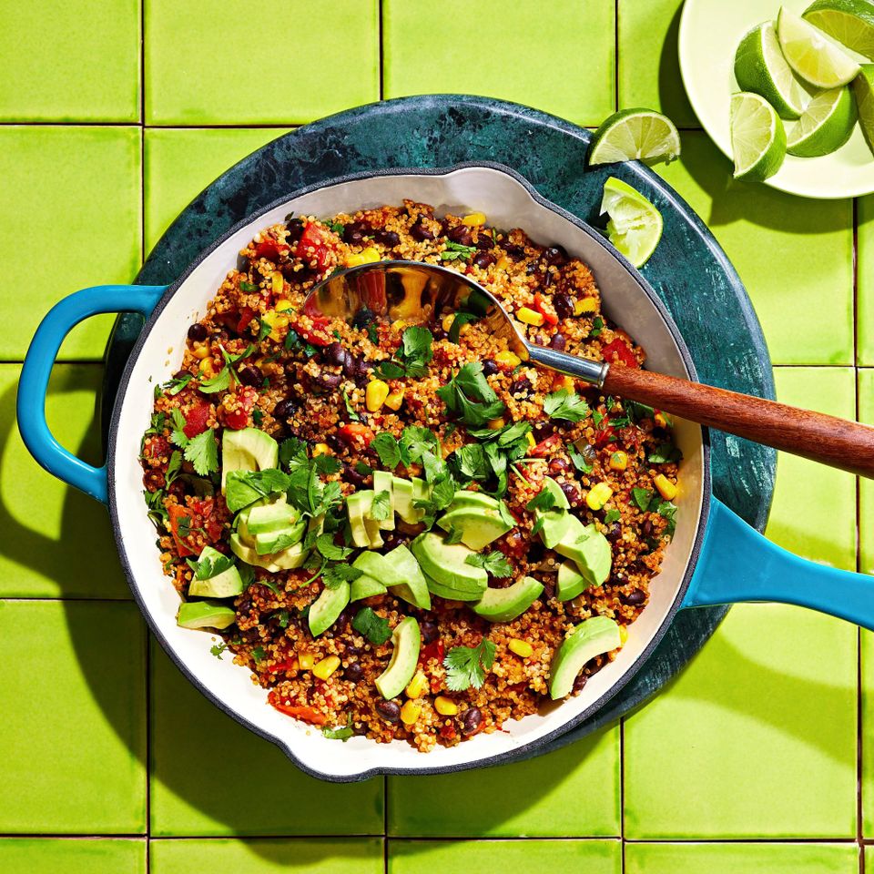 Black beans, tomatoes, and quinoa topped with avocado and fresh herbs in a turquoise skillet
