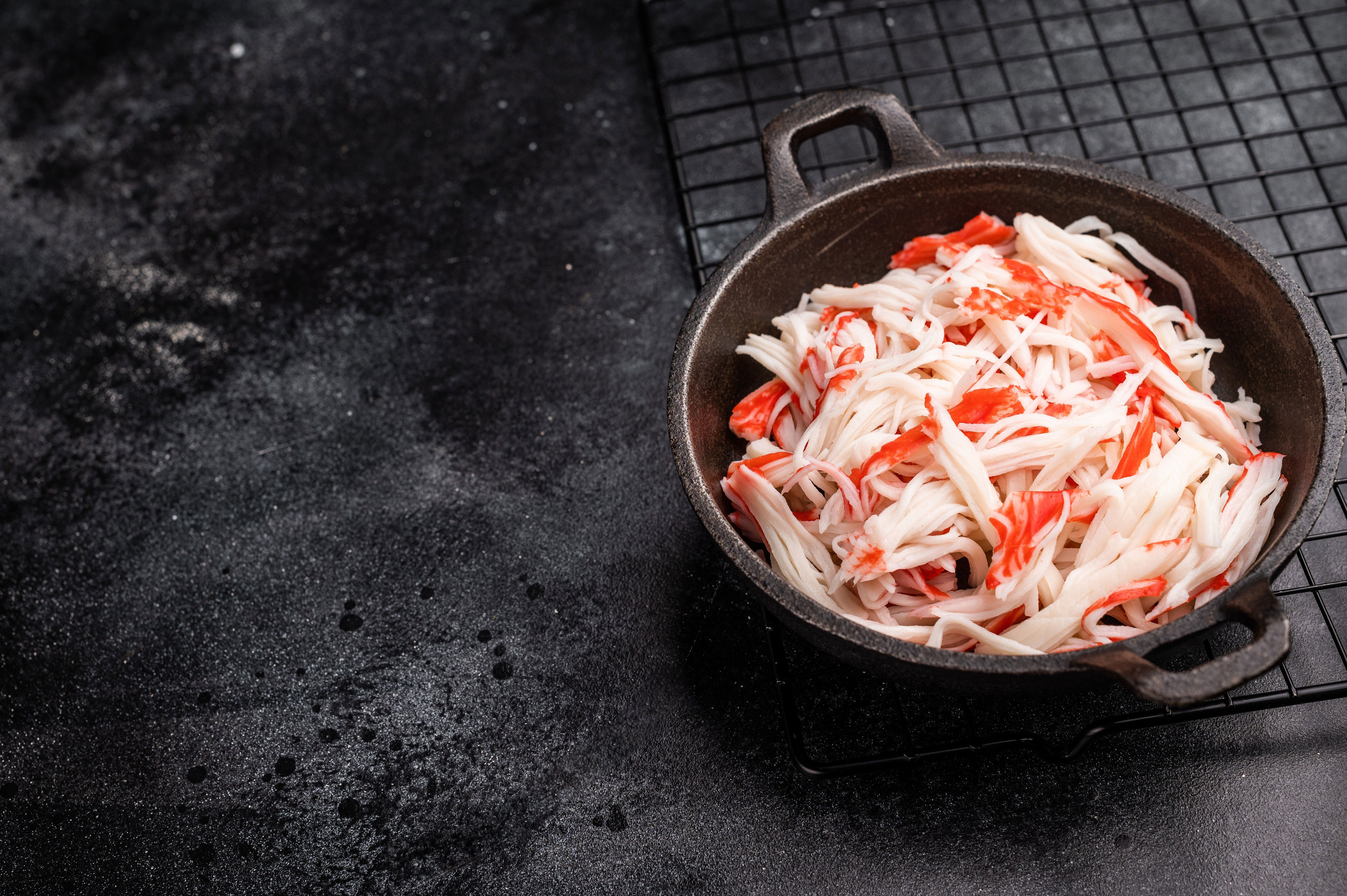 Crab sticks in a black bowl on a wire cooling rack, set against a dark stone background